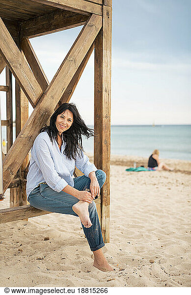 Smiling woman sitting on lifeguard hut at beach