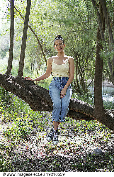 Smiling woman sitting on tree in forest