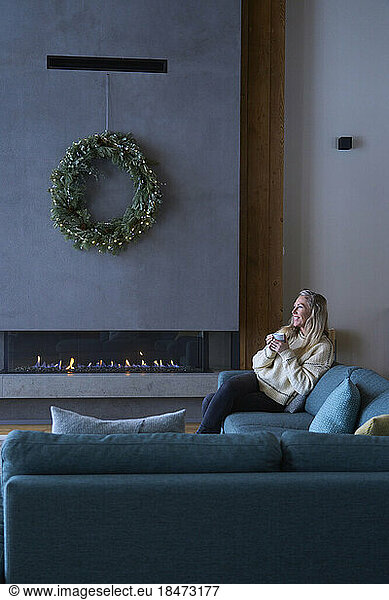 Smiling woman sitting with coffee cup on sofa at chalet