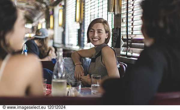 Smiling woman sitting with two friends in a booth in a diner.
