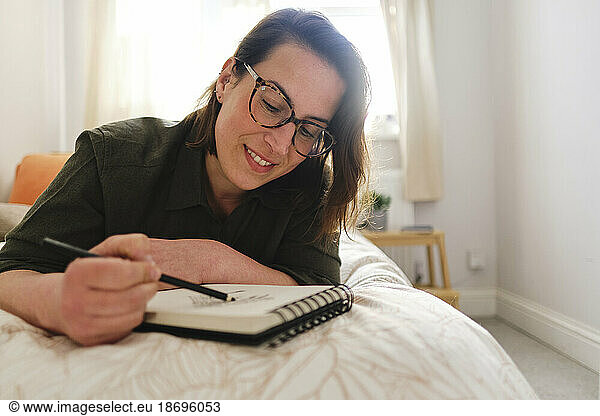 Smiling woman sketching with pencil in bedroom at home
