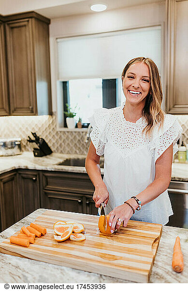 Smiling woman slices an orange on a cutting board in her kitchen