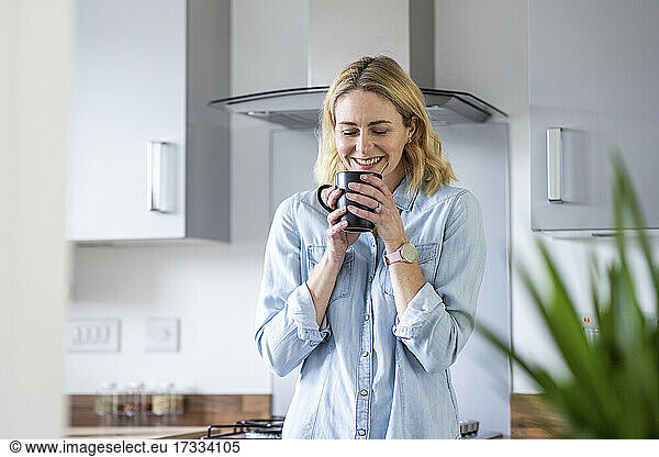 Smiling woman smelling tea in kitchen at home