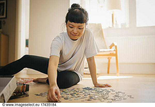 Smiling woman solving jigsaw puzzle on floor in living room at home