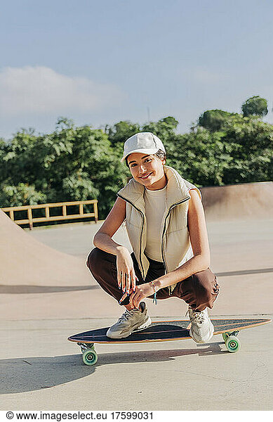 Smiling woman squatting on skateboard in park