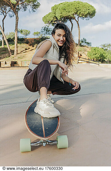 Smiling woman squatting with skateboard in park