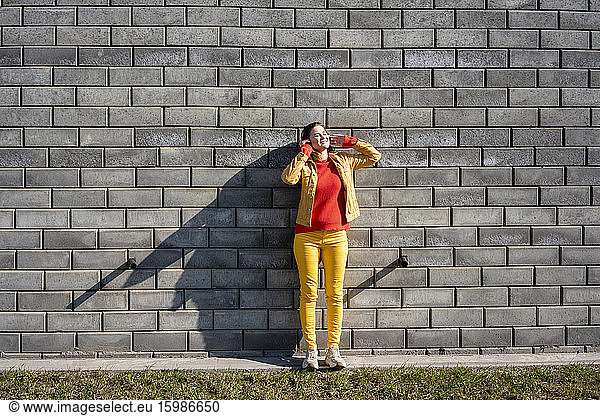 Smiling woman standing at a brick wall listening to music with headphones
