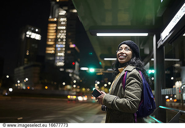smiling woman standing using his cellphone at the bus station