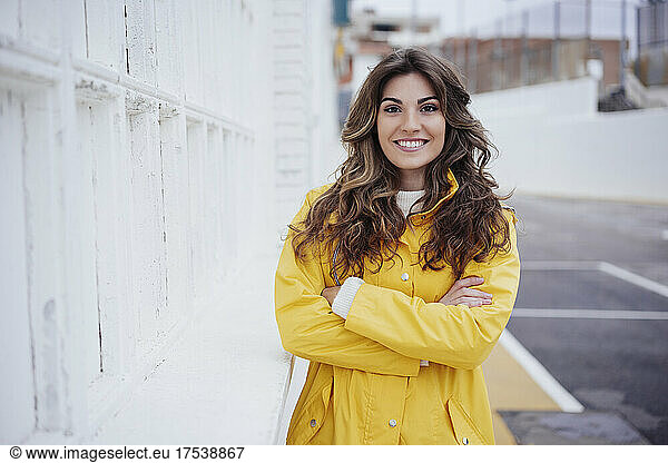 Smiling woman standing with arms crossed by wall