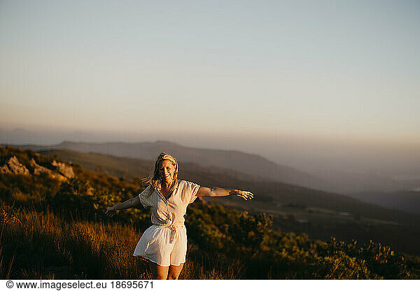 Smiling woman standing with arms outstretched on mountain