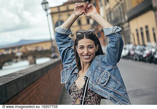 Smiling woman standing with arms raised on city street