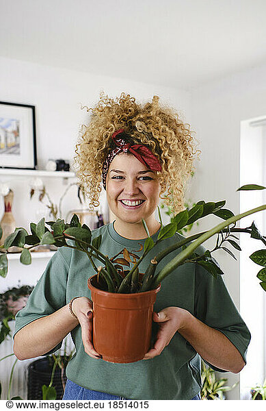 Smiling woman standing with potted plant at home