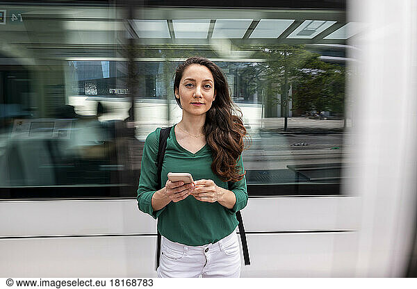 Smiling woman standing with smart phone at tram station