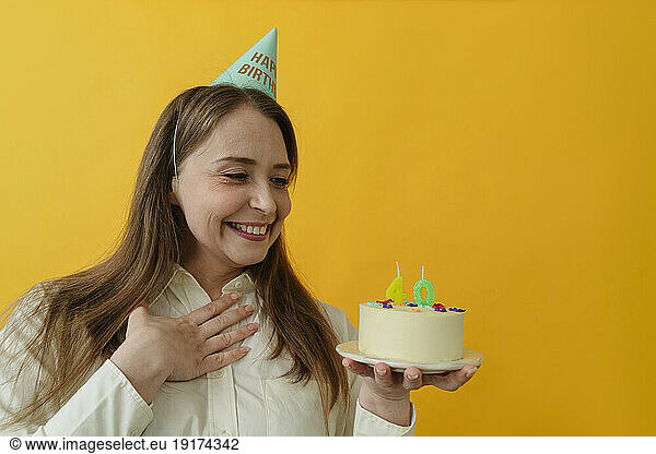Smiling woman staring at birthday cake against yellow background