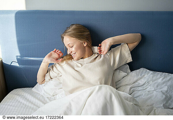 Smiling woman stretching hand while lying on bed at home