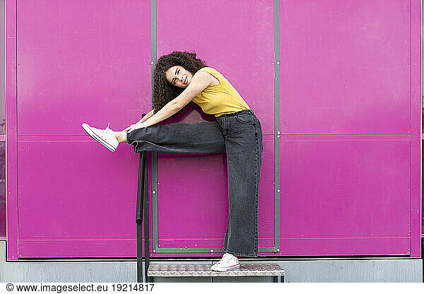 Smiling woman stretching leg in front of pink wall