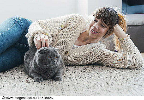Smiling woman stroking cat lying on carpet at home