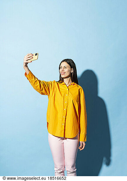 Smiling woman taking selfie standing against blue background
