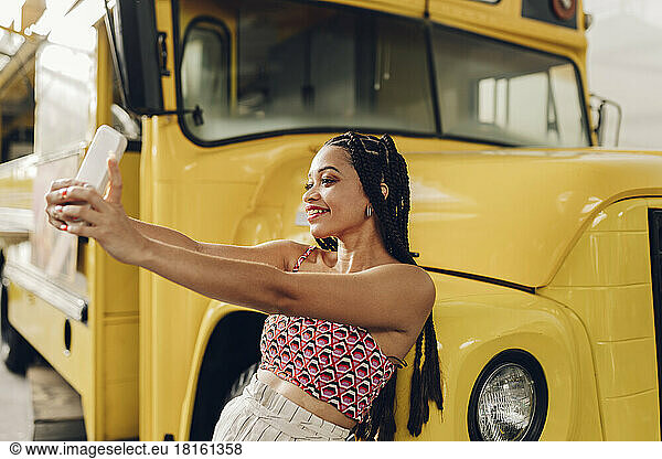 Smiling woman taking selfie through smart phone leaning on food truck