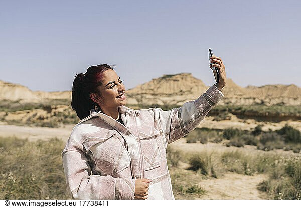 Smiling woman taking selfie through smart phone on sunny day