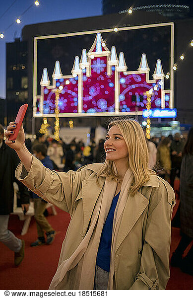 Smiling woman taking selfie through smart phone standing at festival