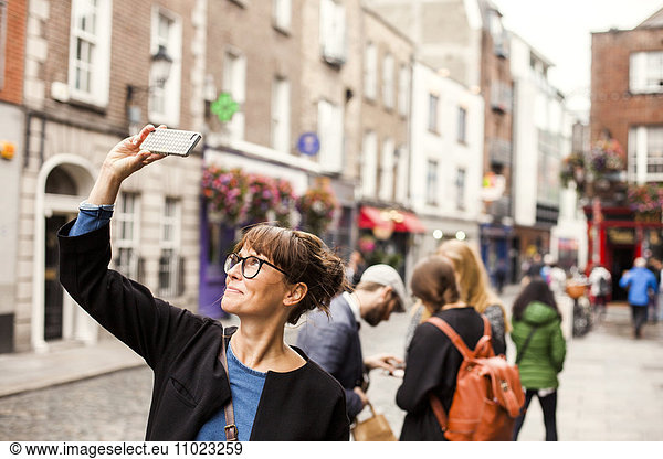 Smiling woman taking selfie with friends standing in background on city street