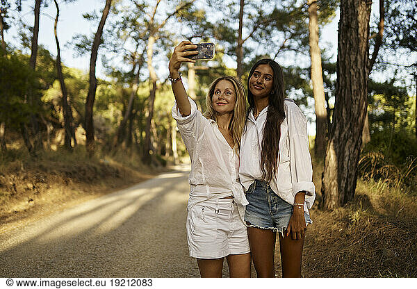 Smiling woman taking selfie with teenage daughter in forest