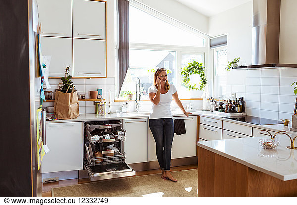 Smiling woman talking on mobile phone while standing in kitchen