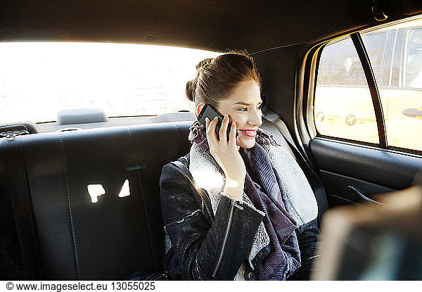 Smiling woman talking on mobile phone while travelling in car