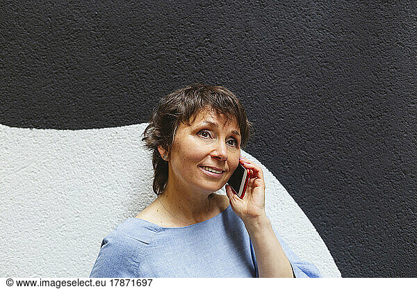 Smiling woman talking on phone in front of wall