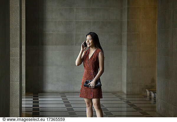 Smiling woman talking on phone while standing at corridor