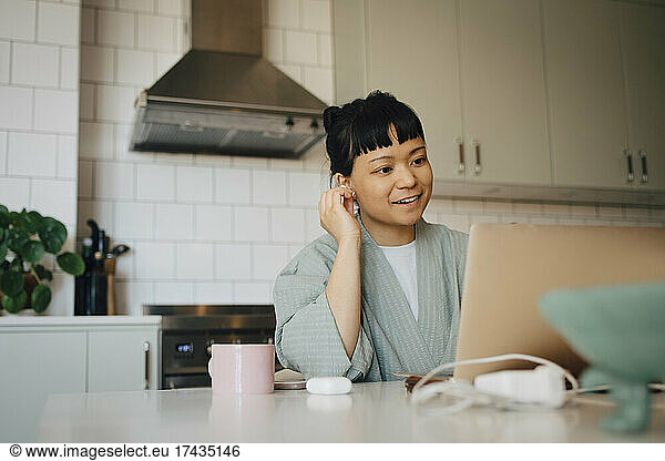 Smiling woman talking on video call through laptop in domestic kitchen