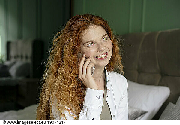 Smiling woman talking through smart phone on bed at home