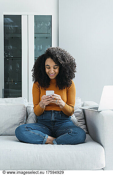 Smiling woman text messaging through mobile phone at home