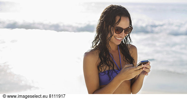 Smiling woman text messaging with cell phone on beach