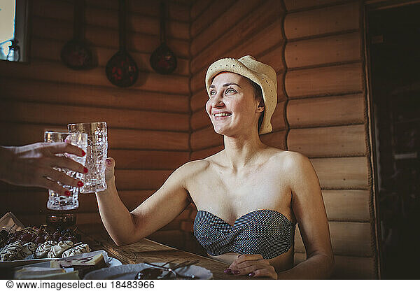 Smiling woman toasting glass with friend in sauna
