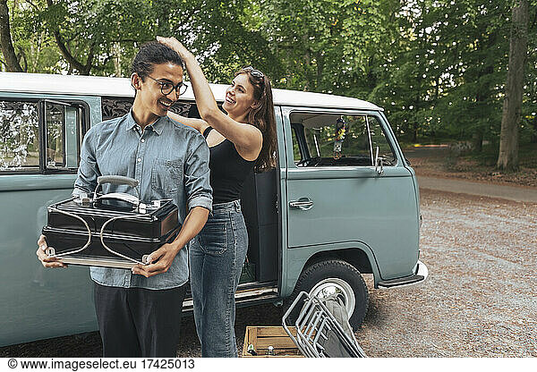 Smiling woman touching male friend's hair outside camping van