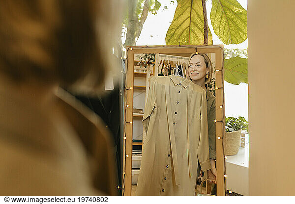 Smiling woman trying on dress and looking at mirror in store