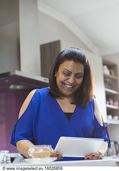 Smiling woman using digital tablet in kitchen