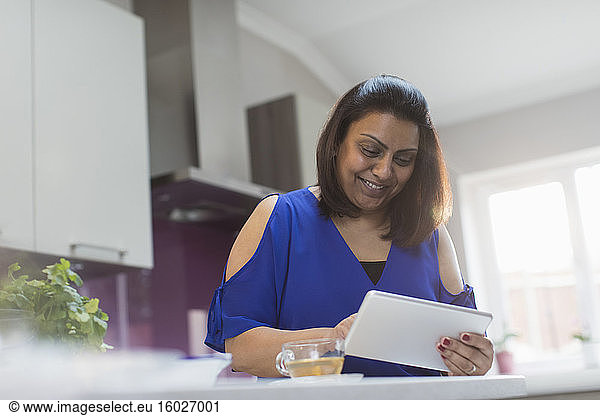 Smiling woman using digital tablet in kitchen