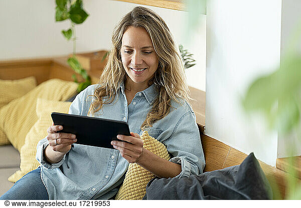 Smiling woman using digital tablet while sitting on couch in living room at home