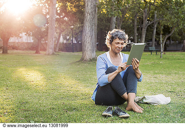 Smiling woman using digital tablet while sitting on grassy field