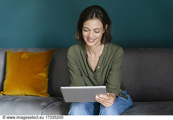Smiling woman using digital tablet while sitting on sofa in living room