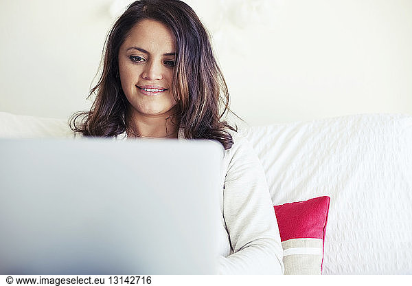 Smiling woman using laptop in bedroom