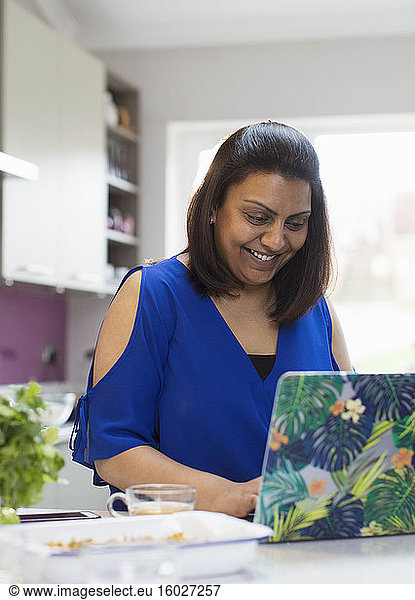Smiling woman using laptop in kitchen