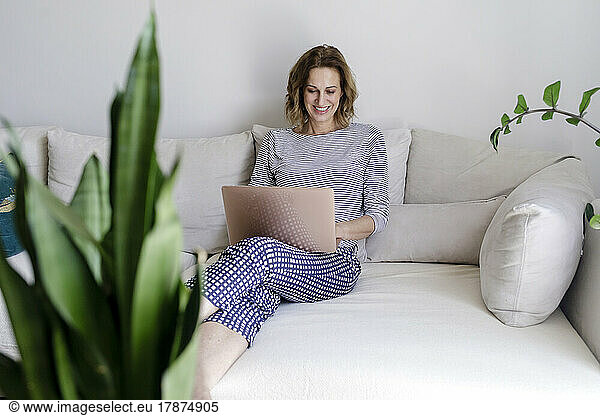 Smiling woman using laptop sitting on couch at home