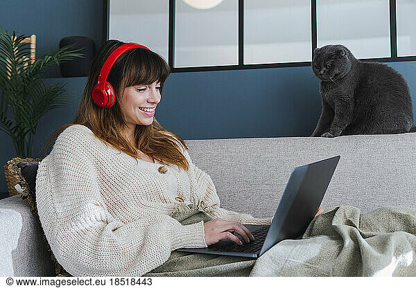 Smiling woman using laptop sitting on sofa at home