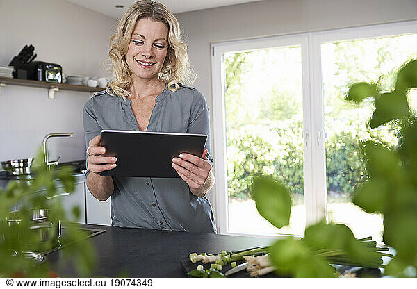 Smiling woman using tablet in kitchen