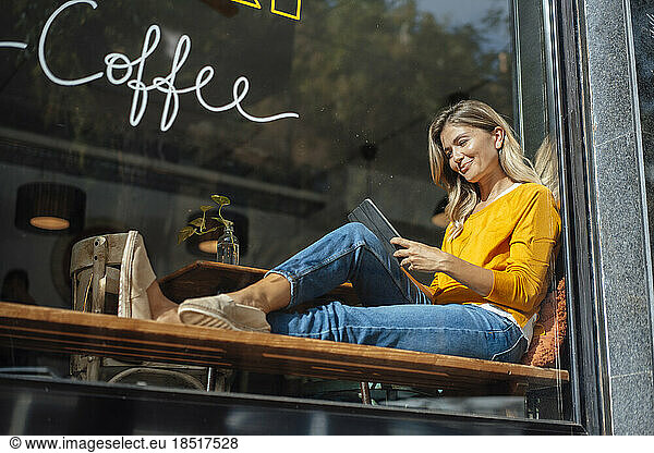 Smiling woman using tablet PC in cafe seen through glass