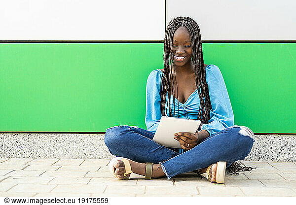 Smiling woman using tablet PC in front of wall